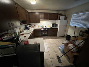 Kitchen featuring dark wood finish cabinetry, black appliances, light countertops, and light tile patterned floors