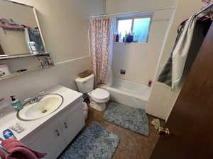 Full bath featuring tile walls, vanity, wainscoting, shower / tub combo, and dark tile patterned flooring