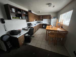 Kitchen with light countertops, freestanding refrigerator, a desk, light tile patterned flooring, and a textured ceiling