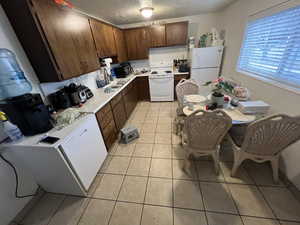 Kitchen featuring light countertops, white appliances, light tile patterned flooring, dark wood finish cabinetry, and a textured ceiling