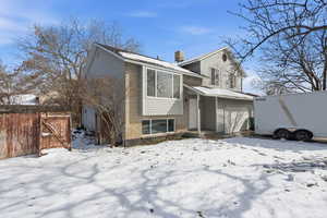 Snow covered house with brick siding, an attached garage, and a gate