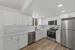 Kitchen with stainless steel appliances, white cabinets, light wood finished floors, light stone counters, and recessed lighting