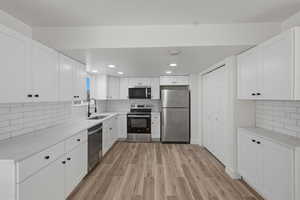 Kitchen featuring tasteful backsplash, stainless steel appliances, white cabinetry, light wood-type flooring, and light stone counters
