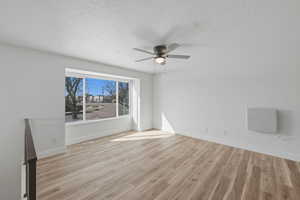 Empty room featuring light wood-style flooring, a ceiling fan, and a textured ceiling