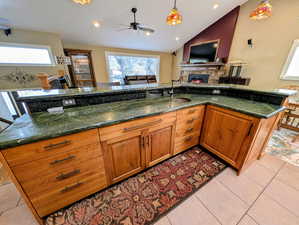 Kitchen featuring wood finish cabinets, a lit fireplace, a ceiling fan, open floor plan, and hanging light fixtures