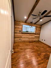 Unfurnished room featuring wooden walls, wood finished floors, a ceiling fan, beamed ceiling, and an accent wall