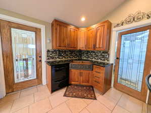 Kitchen featuring wood finish cabinets, backsplash, dark stone countertops, dishwasher, and vaulted ceiling