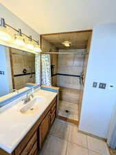 Full bathroom featuring vanity, a stall shower, light tile patterned floors, and a textured ceiling