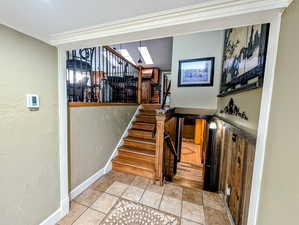 Staircase with a textured wall, crown molding, and tile patterned floors