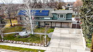 View of front of home with solar panels, concrete driveway, roof with shingles, an attached garage, and a gate