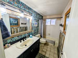 Bathroom featuring wallpapered walls, vanity, shower / tub combo with curtain, a textured ceiling, and light tile patterned floors