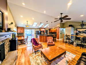 Living area featuring a stone fireplace, light wood finished floors, ceiling fan, and lofted ceiling