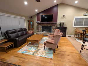 Living area featuring light wood-style flooring, a ceiling fan, a stone fireplace, lofted ceiling, and recessed lighting