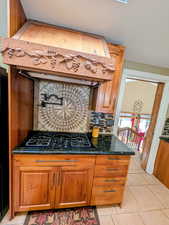 Kitchen with backsplash, dark stone counters, wood finish cabinetry, black gas cooktop, and light tile patterned flooring