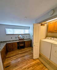 Laundry area featuring light wood-style flooring, cabinet space, a desk, washer and dryer, and a textured ceiling
