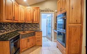 Kitchen with double oven, wood finish cabinets, decorative backsplash, dark stone counters, and light tile patterned floors