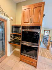Kitchen view of stainless steel double oven, black microwave, dark stone countertops, and a smoke detector