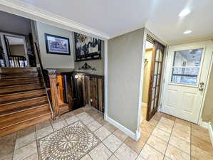 Foyer entrance with crown molding, light tile patterned flooring, a textured wall, and recessed lighting