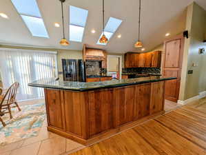 Kitchen with dark stone countertops, black fridge, pendant lighting, tasteful backsplash, and vaulted ceiling
