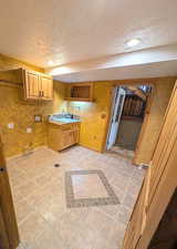 Kitchen featuring inlaid floor details, a textured ceiling, wood finish cabinetry, light tile patterned floors, and open shelves