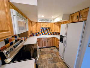 Kitchen with tile counters, white appliances, stone finish floors, backsplash, and recessed lighting