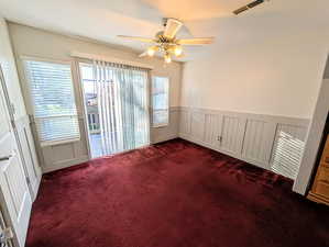 Spare room featuring a wainscoted wall, dark carpet, ceiling fan, and a decorative wall