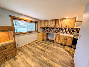 Kitchen featuring stainless steel range with electric cooktop, light wood-style flooring, white microwave, wood finish cabinetry, and decorative backsplash