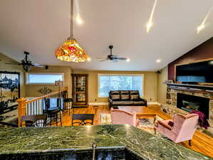 Living area with a ceiling fan, lofted ceiling, a fireplace, and light wood-style flooring