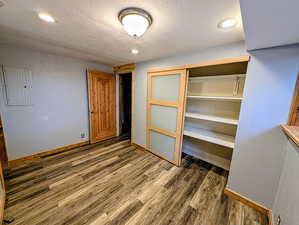 Unfurnished bedroom with a closet, recessed lighting, a textured ceiling, wood finished floors, and electric panel