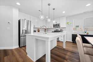 Kitchen featuring stainless steel appliances, white cabinetry, dark wood-style flooring, a kitchen island with sink, and light stone counters