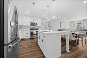 Kitchen with stainless steel appliances, white cabinetry, open floor plan, a kitchen island with sink, and dark wood-type flooring