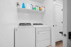 Laundry room with washer and clothes dryer and light wood-style floors