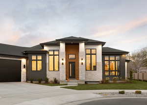 Prairie-style home featuring stone siding, driveway, a garage, a front yard, and roof with shingles