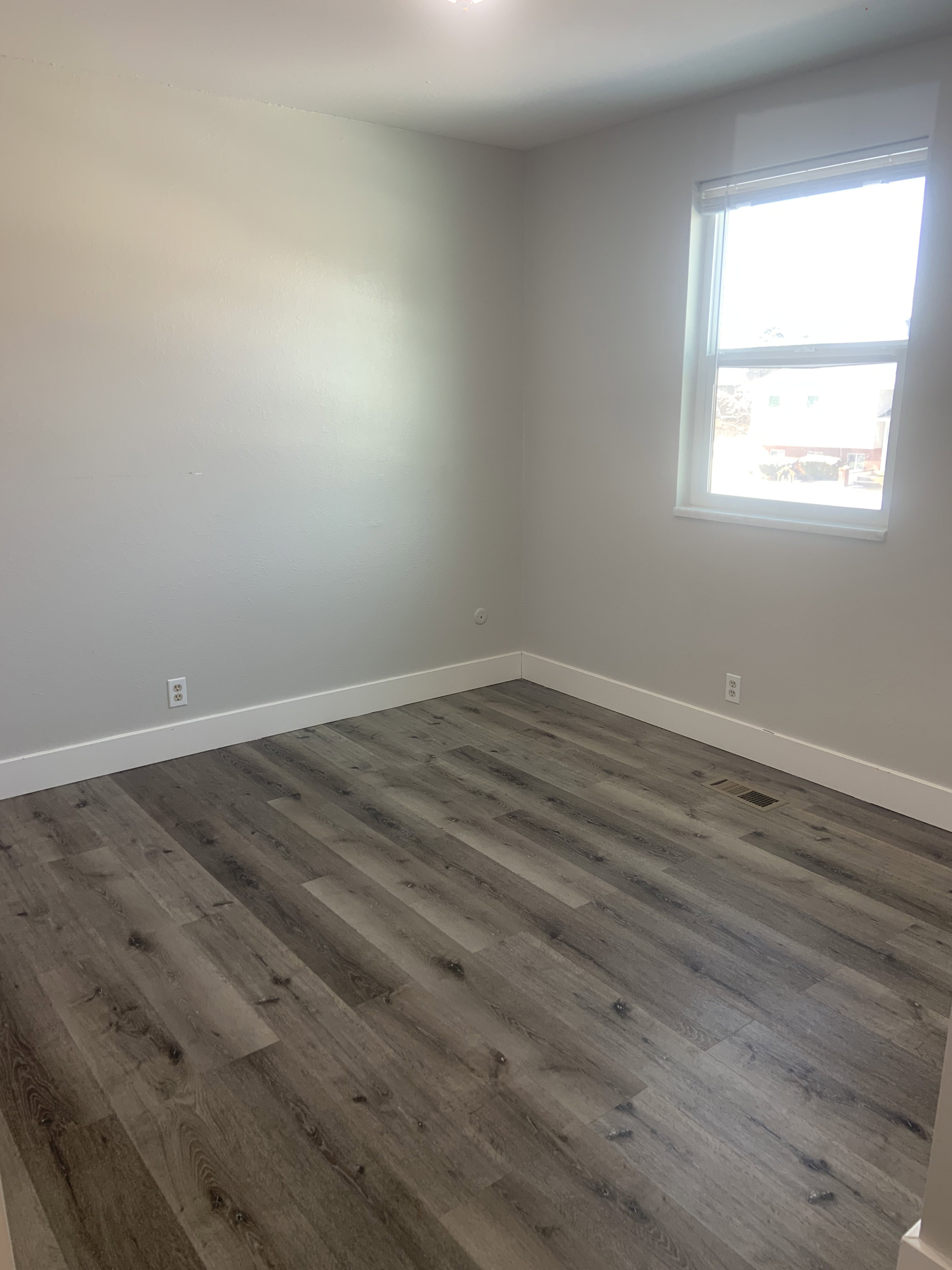 Room featuring wood-finish flooring, white baseboards, and a single window with a white frame