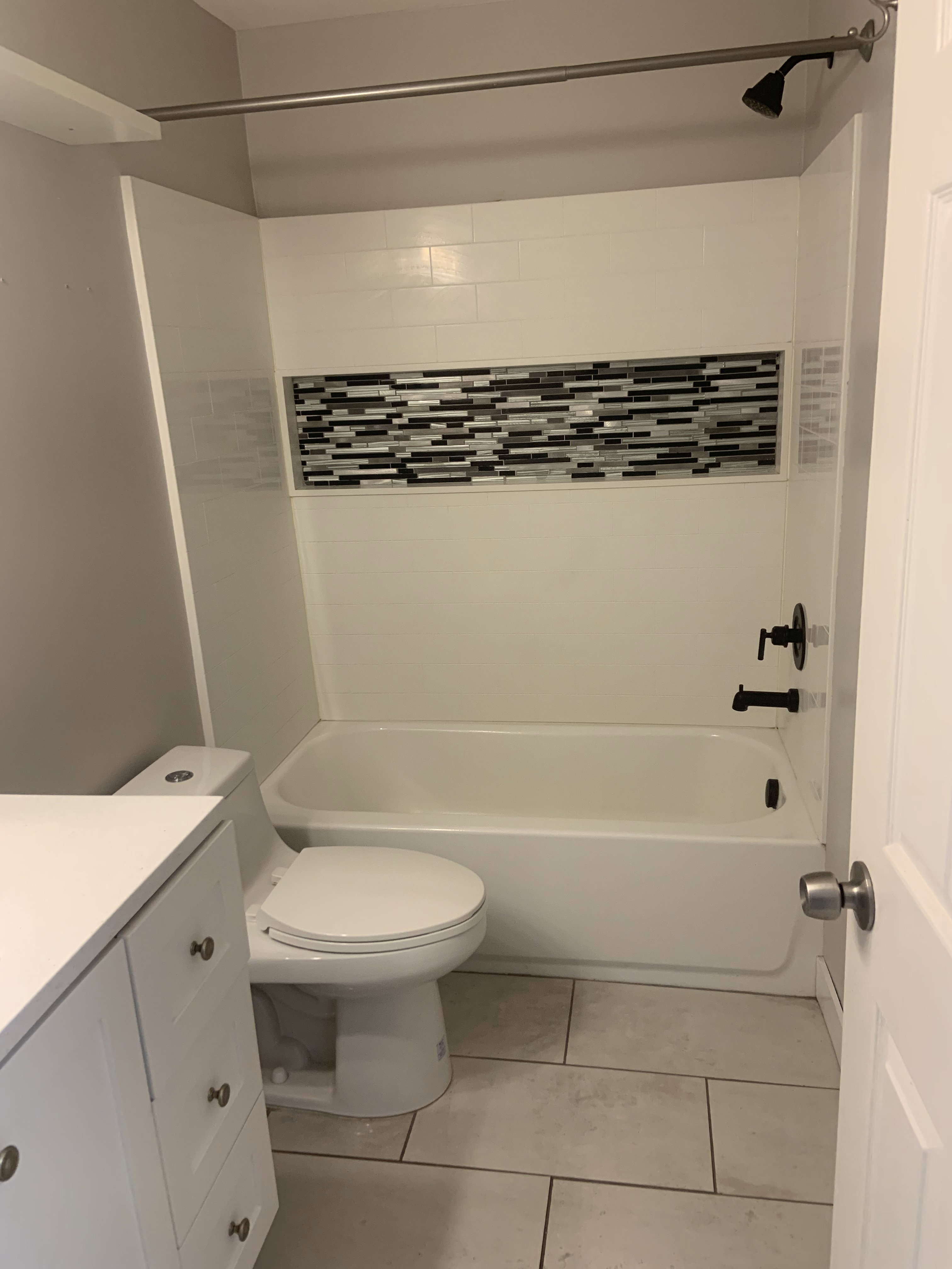 Bathroom featuring a white bathtub, subway tile surround with mosaic accent, and matte black fixtures
