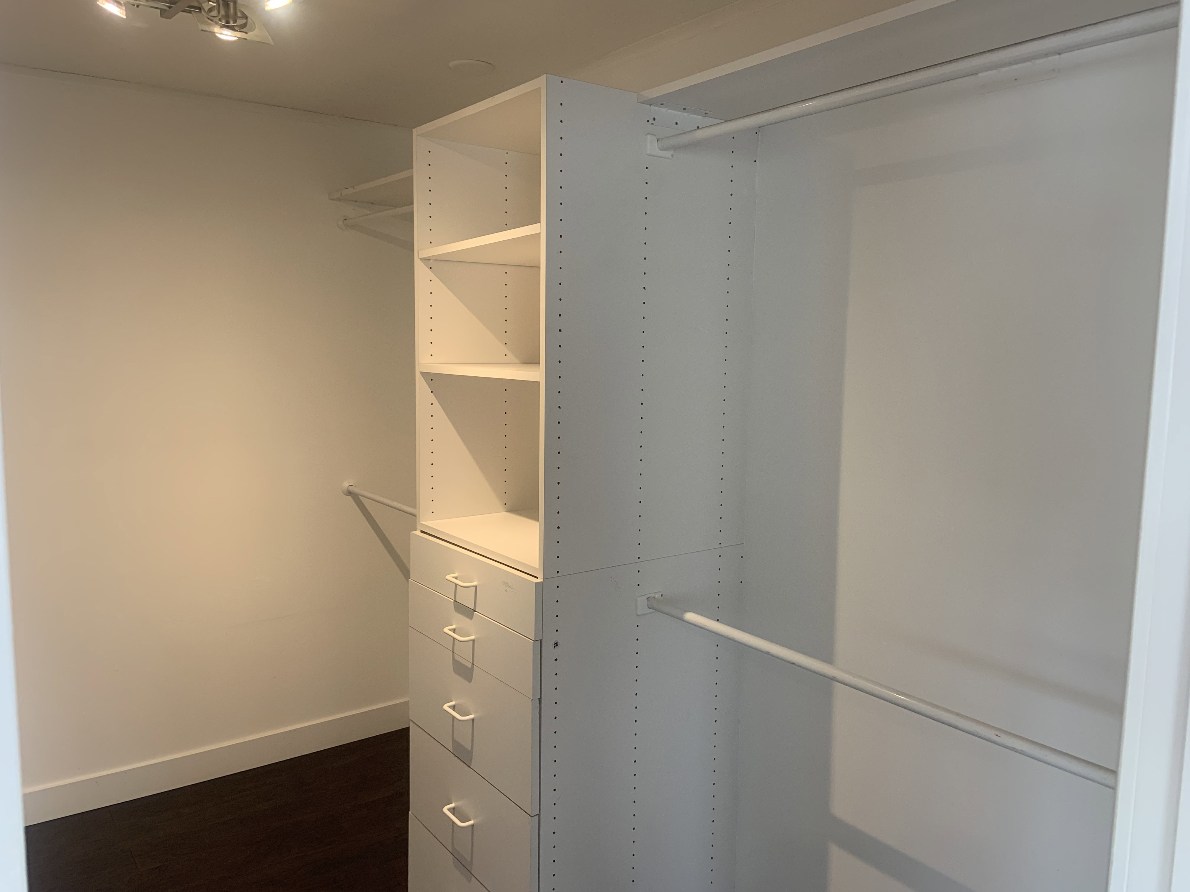 Walk-in closet featuring custom white cabinetry with integrated shelving and drawers, multiple hanging rods, and dark wood-finish flooring