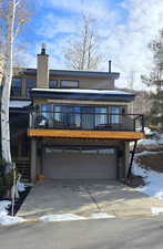 View of front of home with a chimney, concrete driveway, a garage, and a wooden deck
