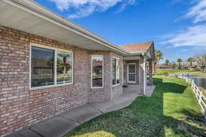 View of side of property featuring a lawn, brick siding, and a patio
