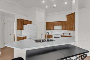 Kitchen with white appliances, crown molding, light countertops, wood finish cabinetry, and a center island with sink