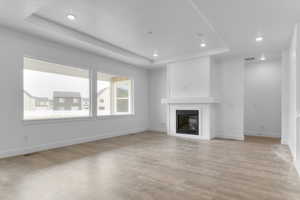 Unfurnished living room featuring a raised ceiling, a glass covered fireplace, recessed lighting, and light wood-style floors