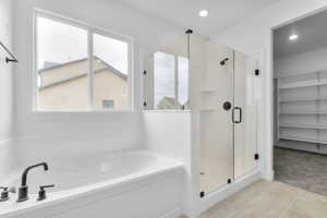 Bathroom with a walk in closet, a shower stall, light carpet, a garden tub, and light tile patterned floors