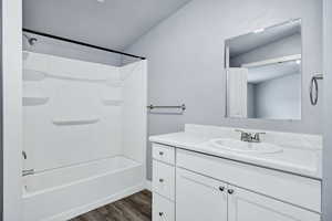 Bathroom with vanity, dark wood finished floors, bathtub / shower combination, and lofted ceiling