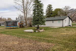 View of grassy yard featuring a patio area, a trampoline, and a playground