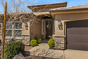 View of exterior entry with stone siding, stucco siding, an attached garage, and a tiled roof