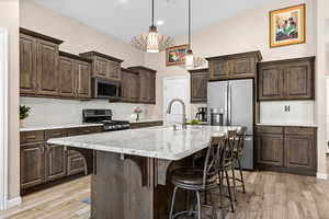 Kitchen featuring backsplash, dark wood finish cabinetry, stainless steel appliances, a kitchen island with sink, and vaulted ceiling
