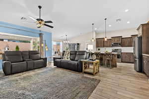 Living room featuring hanging lights, ceiling fan, vaulted ceiling, and light wood-type flooring