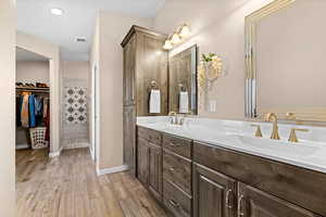 Bathroom featuring double vanity, light wood-style floors, and a walk in closet