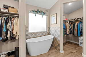 Full bath with a spacious closet, a freestanding bath, light wood-style flooring, and tile walls
