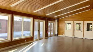 Empty room featuring healthy amount of natural light, wooden walls, wood-type flooring, a vaulted wood ceiling, and french doors