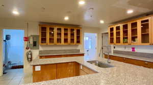 Kitchen with glass insert cabinets, electric panel, light stone countertops, recessed lighting, and light tile patterned flooring